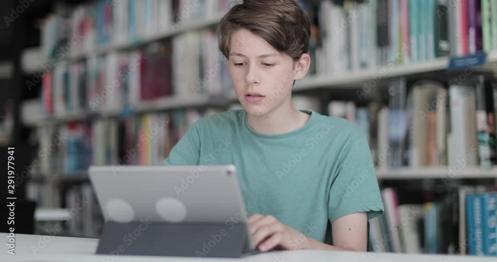 High school male student studying with digital tablet in library High school male student studying with digital tablet in library