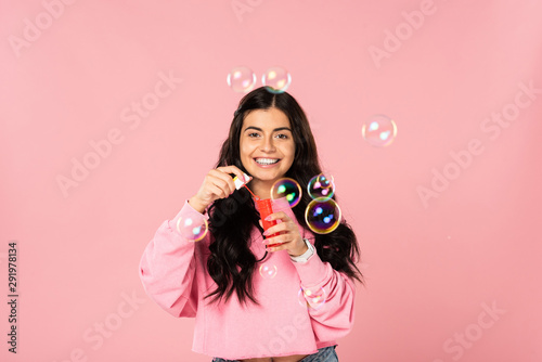 beautiful girl playing with soap bubbles isolated on pink