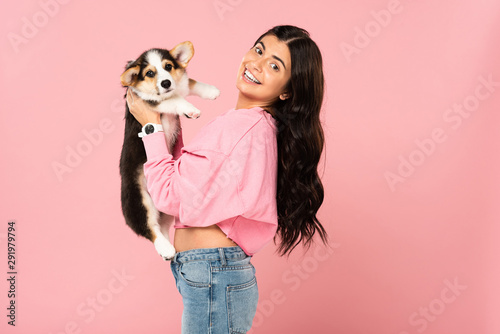 smiling woman holding Welsh Corgi puppy, isolated on pink