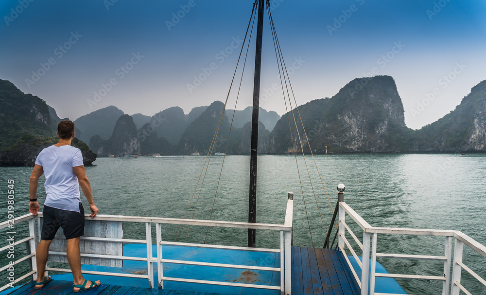 Man is standing on the boat. He is alone in the middle of Halong Bay, Vietnam. One of the most popular tourist destinations. Misty rock formations are on a background. He is having a good body.