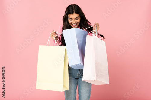attractive smiling girl holding shopping bags, isolated on pink