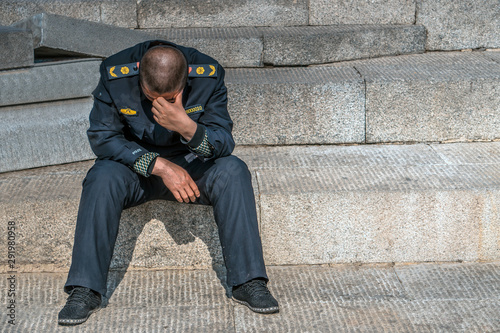 Fototapeta Sad policeman is sitting on the floor with his had down, he lost his job, he is alone