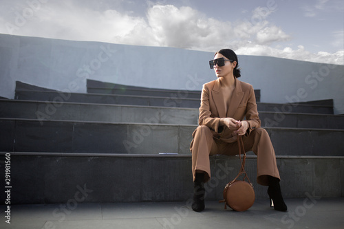 Fashion portrait of a successful business woman sitting on stairs. City background