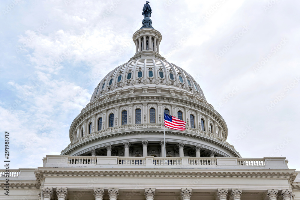 Obraz premium The Dome - A low-angle close-up view of a U.S. national flag flying at front of the dome of the Capitol Building. Washington, D.C., USA. 