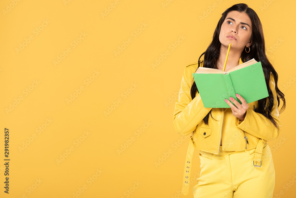 pensive girl holding pencil and book, isolated on yellow pensive girl holding pencil and book, isolated on yellow