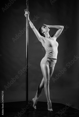 Beautiful athletic busty elegant blonde girl performs artistic elements of an exotic dance on a gray background. Health, lifestyle, sports black and white monochrome design. Copy space.