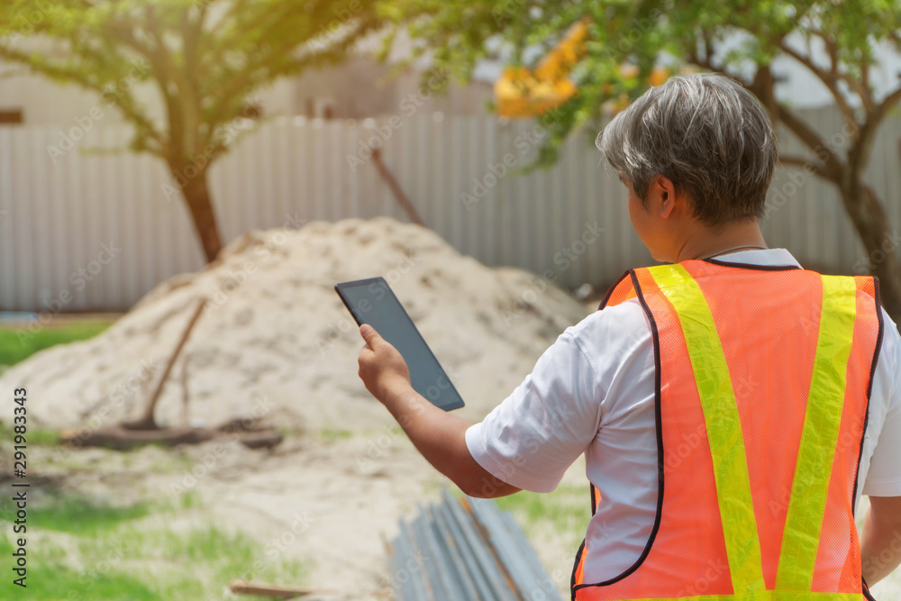 Fototapeta premium Engineering wearing a white safety helmet standing In front of the construction site And using tablet to construction. Concepts for controlling and checking the construction accuracy