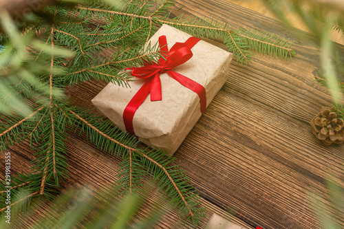 Fur spruce pine coniferous branches, gift box craft paper with red bow on the brown brushed wooden background