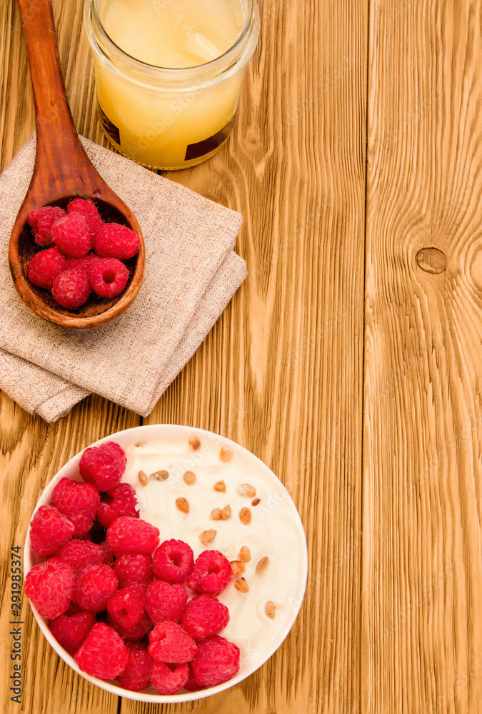 organic products honey, yogurt and raspberries on a light wooden table