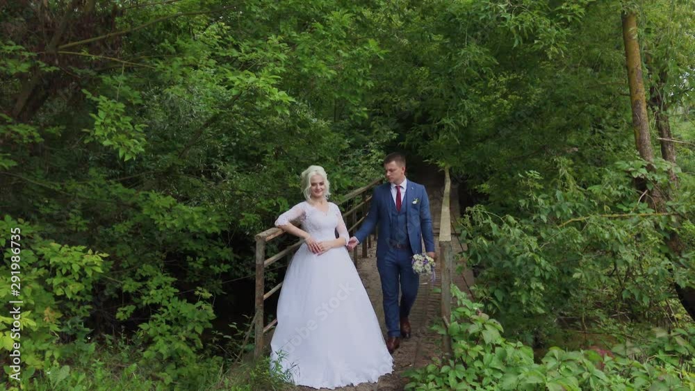 Beautiful bride and groom on an old iron bridge in the forest. Groom caresses his beloved. Beautiful bride and groom on an old iron bridge in the forest. Groom caresses his beloved.