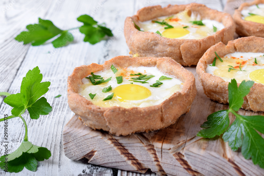 Baked rye tartlets with cheese and quail eggs on white wooden table Baked rye tartlets with cheese and quail eggs on white wooden table