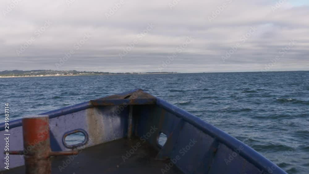 A daylight closeup shot of the front hull of a fast motorboat cruising the calm blue waters of the ocean with the view of the wide horizon and an island seen in the distance.. A daylight closeup shot of the front hull of a fast motorboat cruising the calm blue waters of the ocean with the view of the wide horizon and an island seen in the distance..