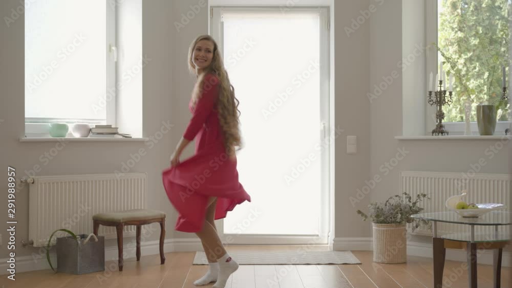 Beautiful smiling caucasian woman with a long curly hair in the red dress dancing at home. Attractive young girl having fun indoors. Beautiful smiling caucasian woman with a long curly hair in the red dress dancing at home. Attractive young girl having fun indoors.