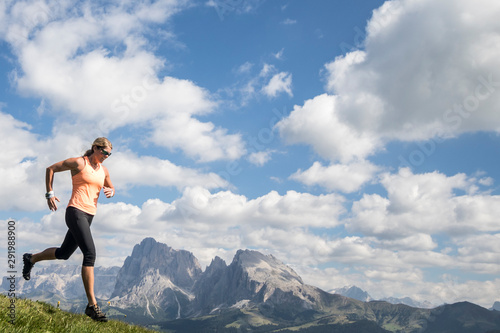 A woman trail runner charges in front of a Dolomites mountainscape
