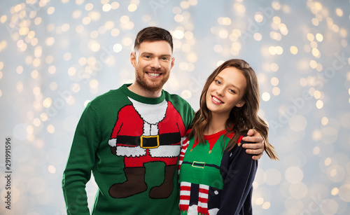 christmas, people and holidays concept - portrait of happy couple at ugly sweater party over festive lights background