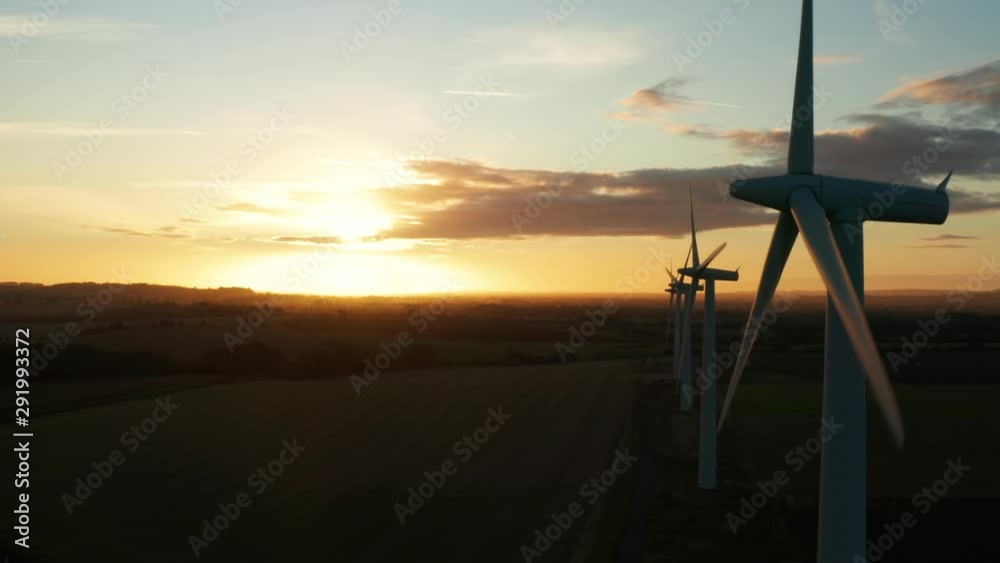 Aerial view across large wind turbines at sunrise on a clear day slowly ...