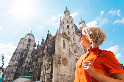 A young woman in a bright orange dress stands on the background of St. Stephen's Cathedral in Vienna, Austria