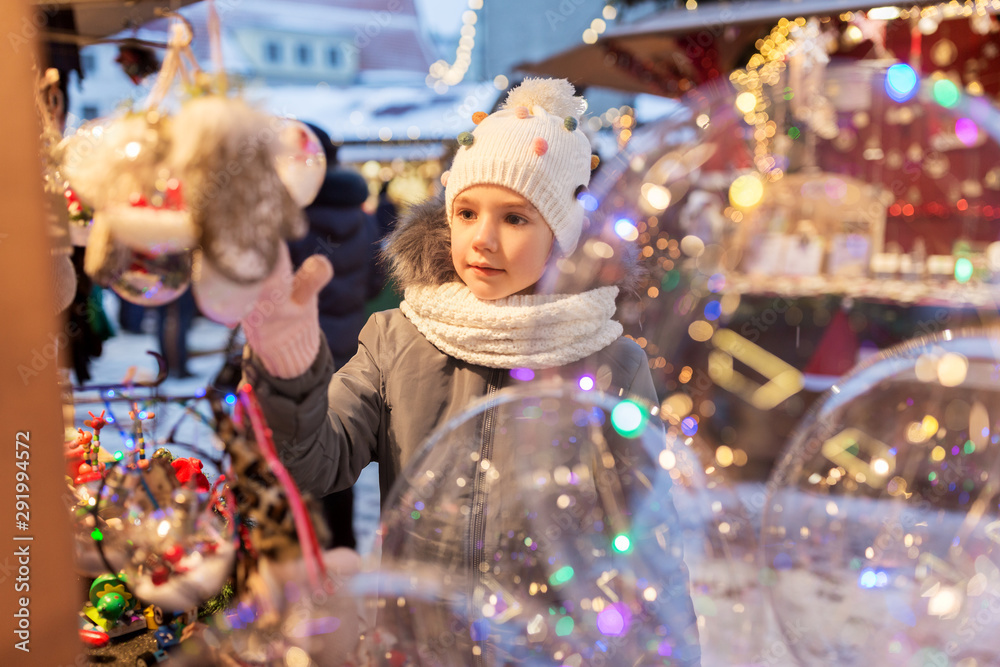 holidays, childhood and people concept - happy little girl choosing christmas balls at market in winter