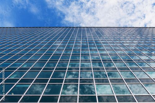 Large facade of a glass building  reflecting white clouds and blue sky.