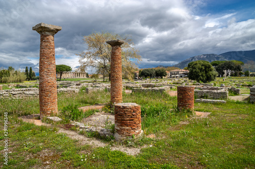 Brick's columns, in the distance - the ancient greek temple of Athena or Temple of Ceres, (c. 500 BC) on a cloudy and sunny spring day in Archaeological Park of Paestum