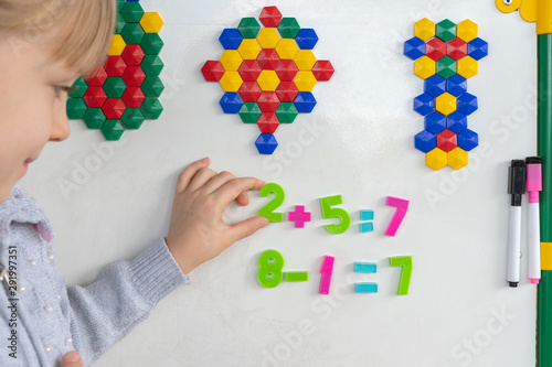 Little preschooler girl on magnetic interactive white borad is studying addition and subtraction in math lesson. Education School Preschool concept.