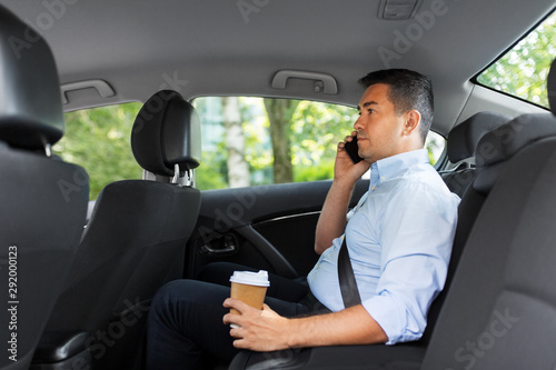 transport, business and communication concept - businessman drinking takeaway coffee and calling on smartphone on back seat of taxi car
