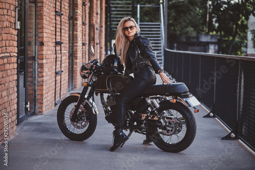 Sexy dramatic woman is parking her shiny new motorbike next to brick wall.