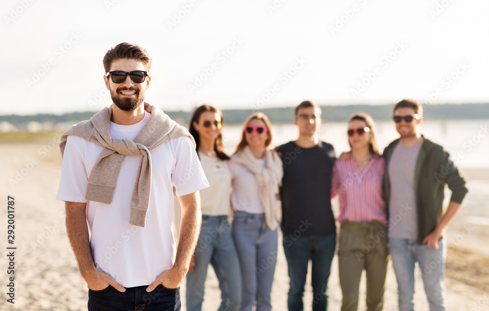 Obraz premium friendship, leisure and people concept - happy man with group of friends on beach in summer