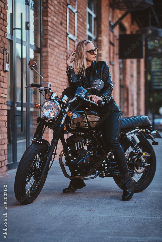 There are sexy mature woman in sunglasses and black leather clothing on the bike.