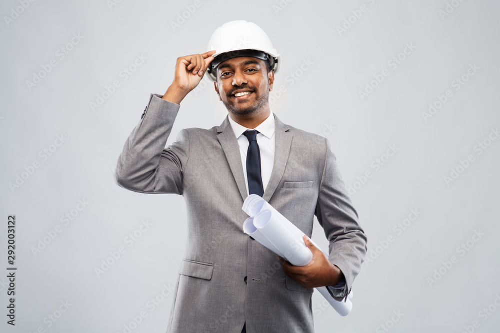 architecture, construction business and people concept - smiling indian male architect in helmet with blueprints over grey background architecture, construction business and people concept - smiling indian male architect in helmet with blueprints over grey background