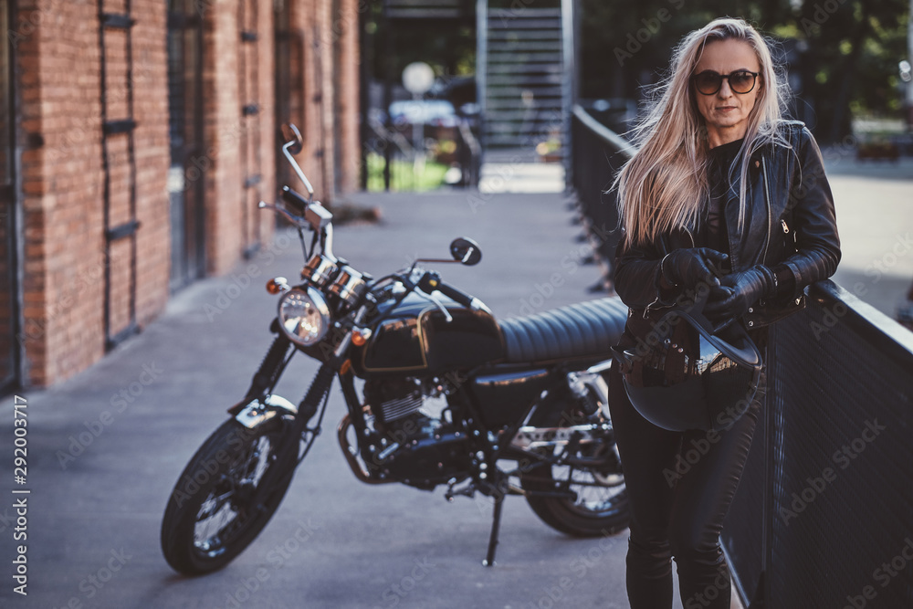 Sexy blond woman is posing for photographer while standing next to her bike.