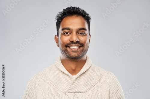 emotion, expression and people concept - smiling indian man in knitted woollen sweater over gray background photo