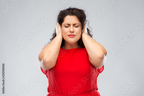 noise, stress and people concept - woman in red dress with closed eyes closing her ears by hands over grey background