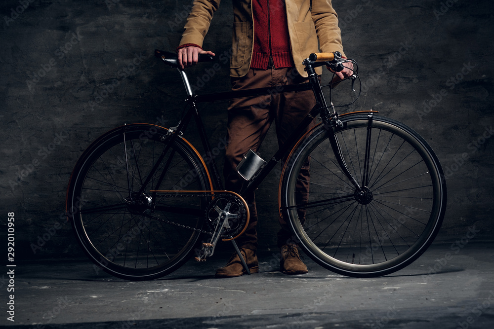 Naklejka premium Man with his bicycle is posing for photographer at dark photo studio.