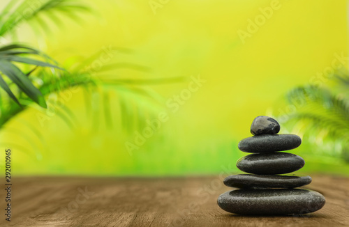 Table with stack of stones and blurred green leaves on background, space for text. Zen concept
