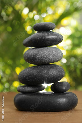 Stack of stones on wooden table against blurred green background  closeup. Zen concept