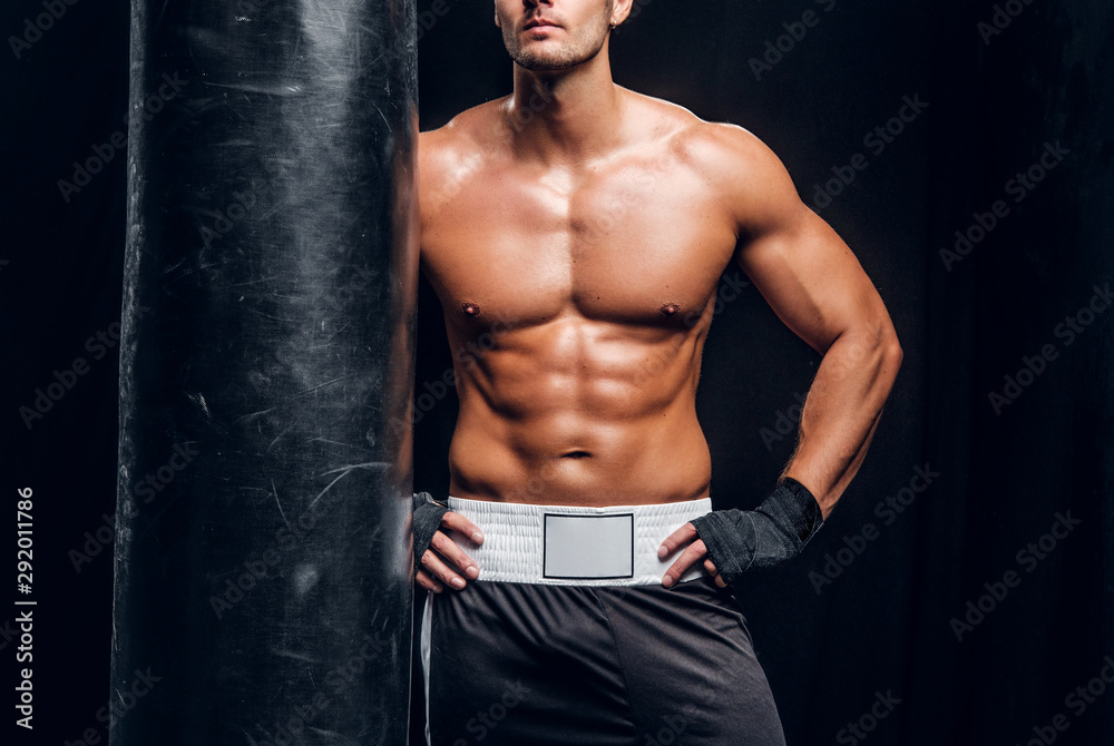Attractive sporty man is posing with punching bag in dark photo studio. Attractive sporty man is posing with punching bag in dark photo studio.