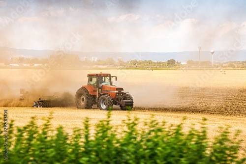 Tractor ploughing the field in sunset with dust in the air