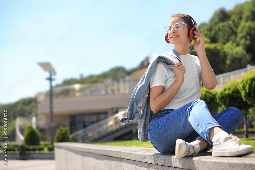 Young woman with headphones listening to music on city street. Space for text