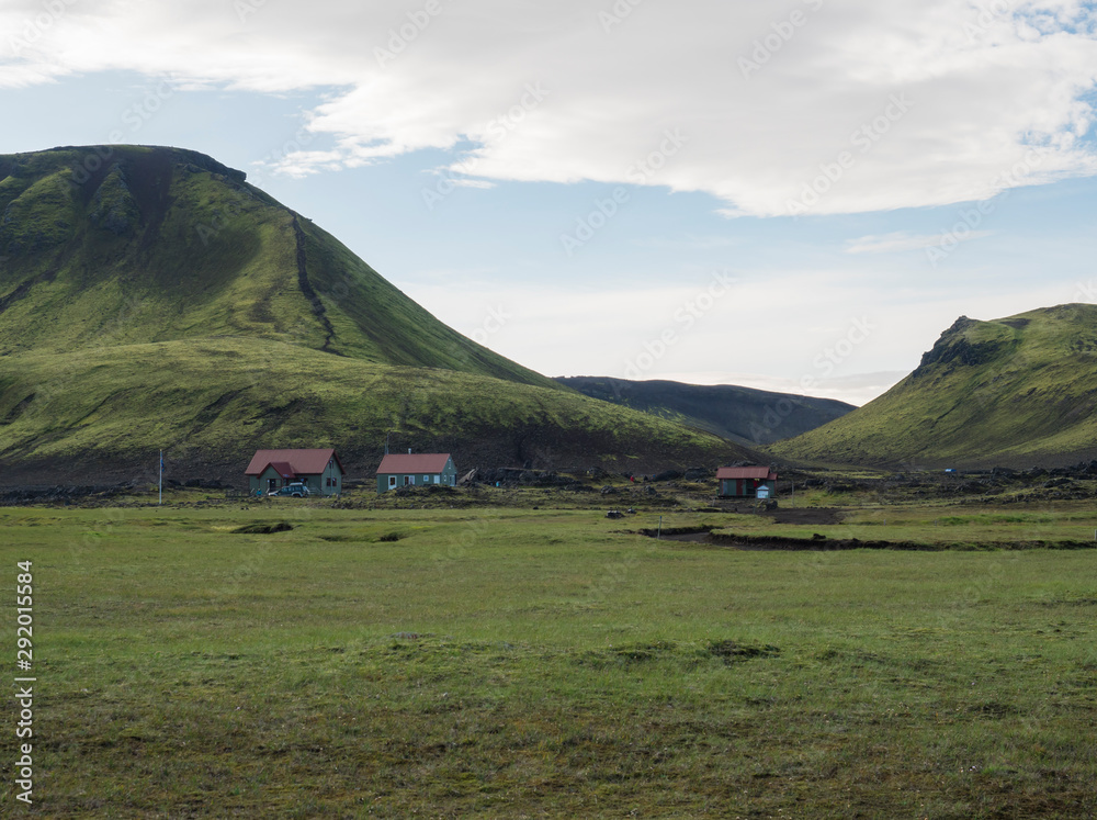 Hvanngil campsite path in lava field and green valley, small houses of hvanngil hut. volcanic mountains volcanic landscape with blue sky, Laugavegur Trail between Emstrur-Botnar and Alftavatn, central