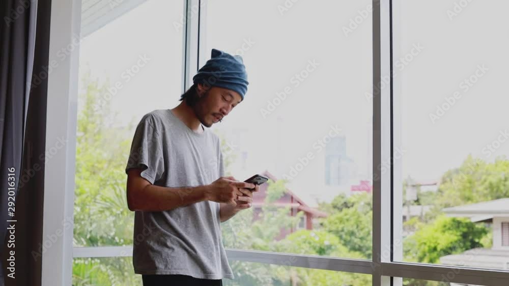 custom made wallpaper toronto digitalHandsome Asian businessman typing a message on his smartphone while standing beside the window in the living room at home.