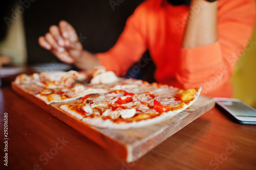 Close up hand of man in orange sweater sitting at pizzeria with pizza.
