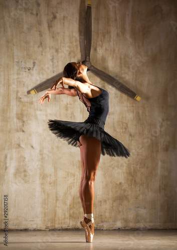 Young beautiful ballerina in black ballet tutu posing in dark studio