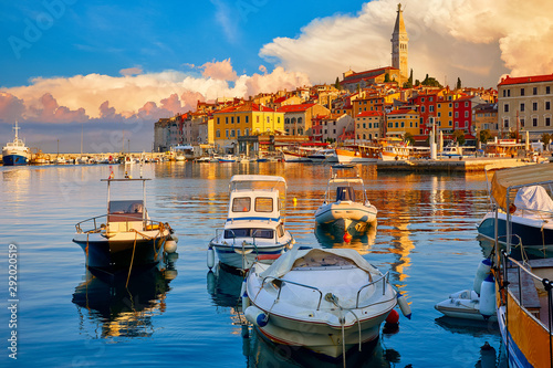 Rovinj, Istria, Croatia. Motorboats and boats on water in port Rovinj. Medieval vintage houses of old town. Yachts landing, high tower of Church of Saint Euphemia. Morning sunrise blue sky withclouds.