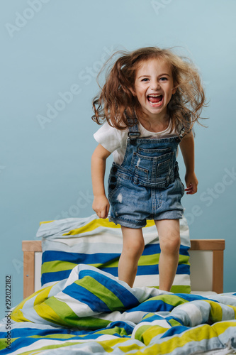 Little girl is playing actively, jumping in bed over blue background. photo