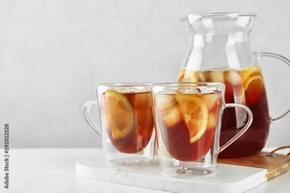 Cups and jug of refreshing iced tea on light table Cups and jug of refreshing iced tea on light table