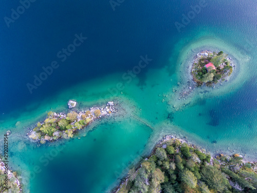 Top down aerial view of small islands in the Eibsee lake with clear blue water, in south Germany