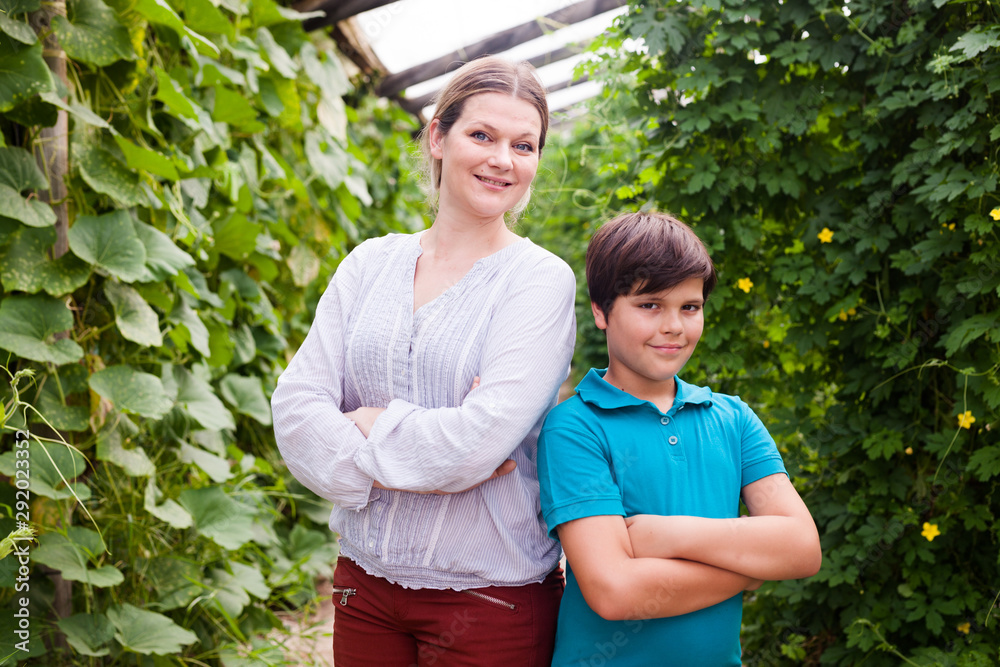 Smiling  boy  with mother standing near seedlings in  greenhouse during gardening