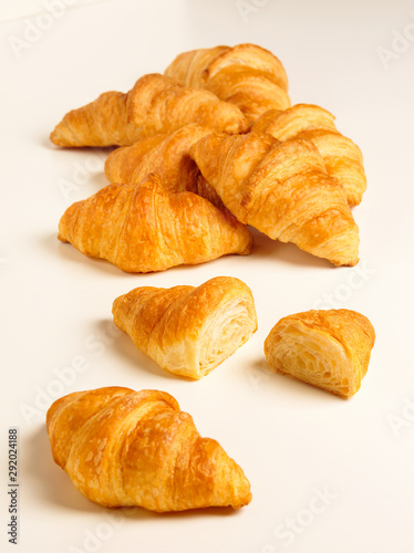 Pile of butter Croissants plus one cut and one whole against white