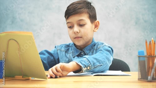 Young concentrated school kid in blue jeans t-shirt writing, copying the text from book on the bookholder, then highlighting the most important things in the copybook. photo